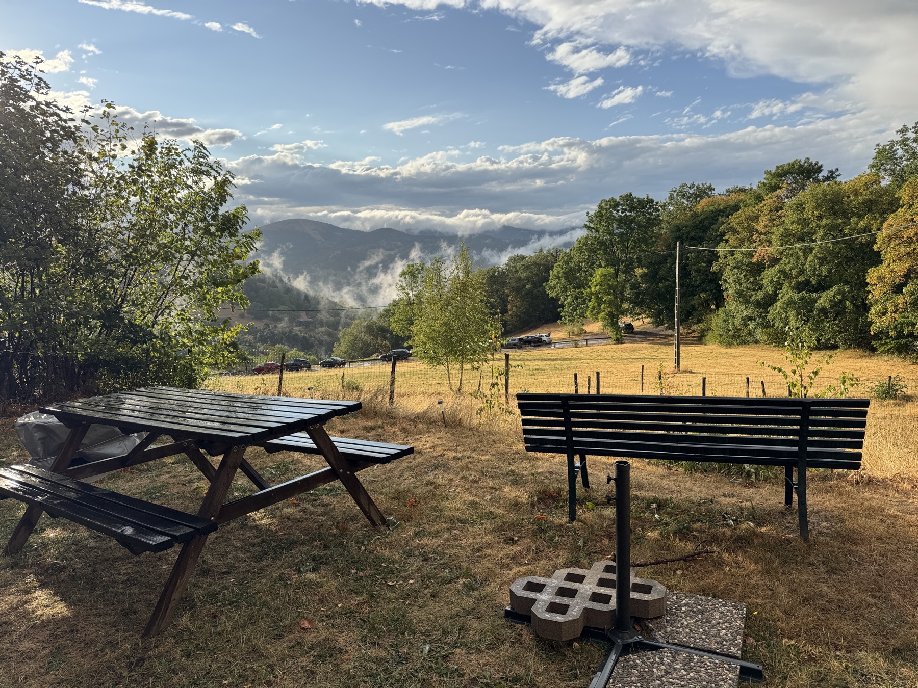 Rastplatz mit Bank und Tisch, Blick über die Wiese in die nebelverhangenen Berge